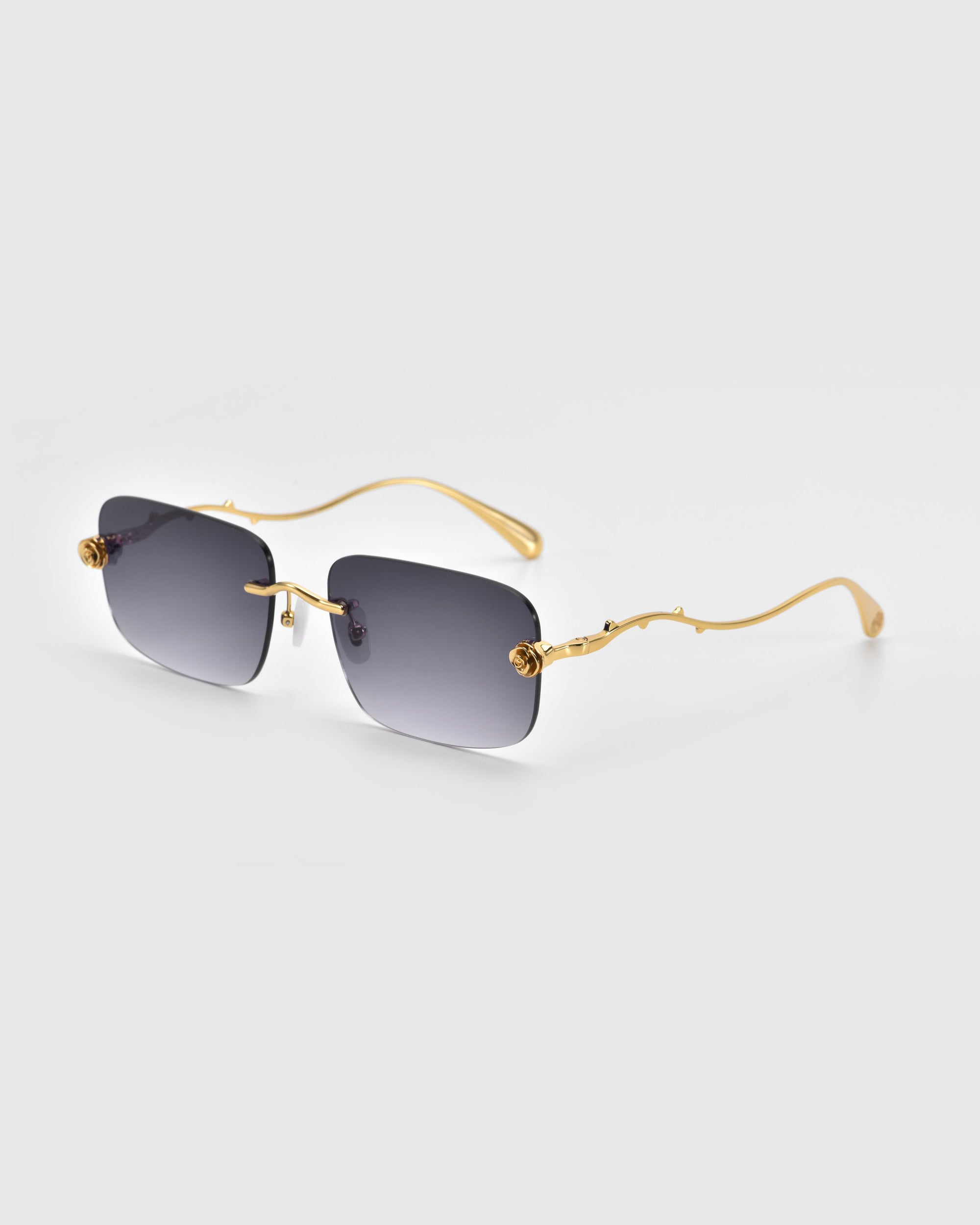 From For Art's Sake® Rose Garden Collection, these sleek sunglasses boast gold-toned intricately designed arms and dark oversized frameless lenses, highlighting a modern and elegant design on a light gray backdrop.