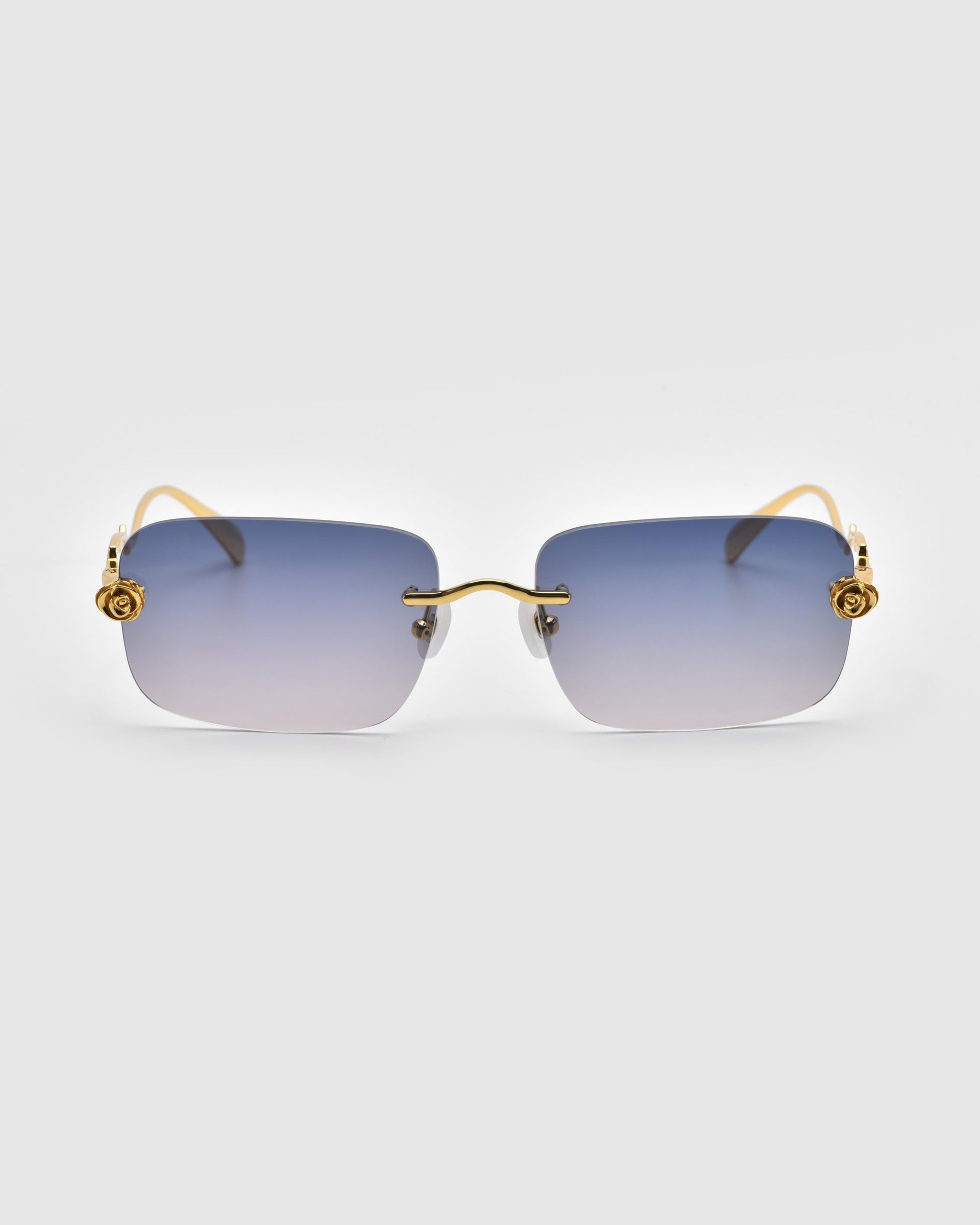 For Art's Sake® Rose Garden sunglasses boast oversized frameless gradient blue lenses, gold-tone temples, and decorative flower accents on the hinges against a plain gray background.