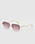 For Art's Sake® Rose Garden sunglasses showcase gold-colored, intricately designed frames with square gradient lenses from pink to light gray. The unique wavy temples have delicate sculpted rose ornaments against a white background.