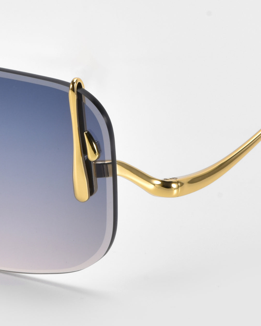 A close-up of For Art's Sake® Vermilion sunglasses showcases gradient blue lenses and a gold frame with artistic flair. The metallic gold temple arm curves elegantly. Sleek, modern lines are enhanced by subtle metal accents against a white background.