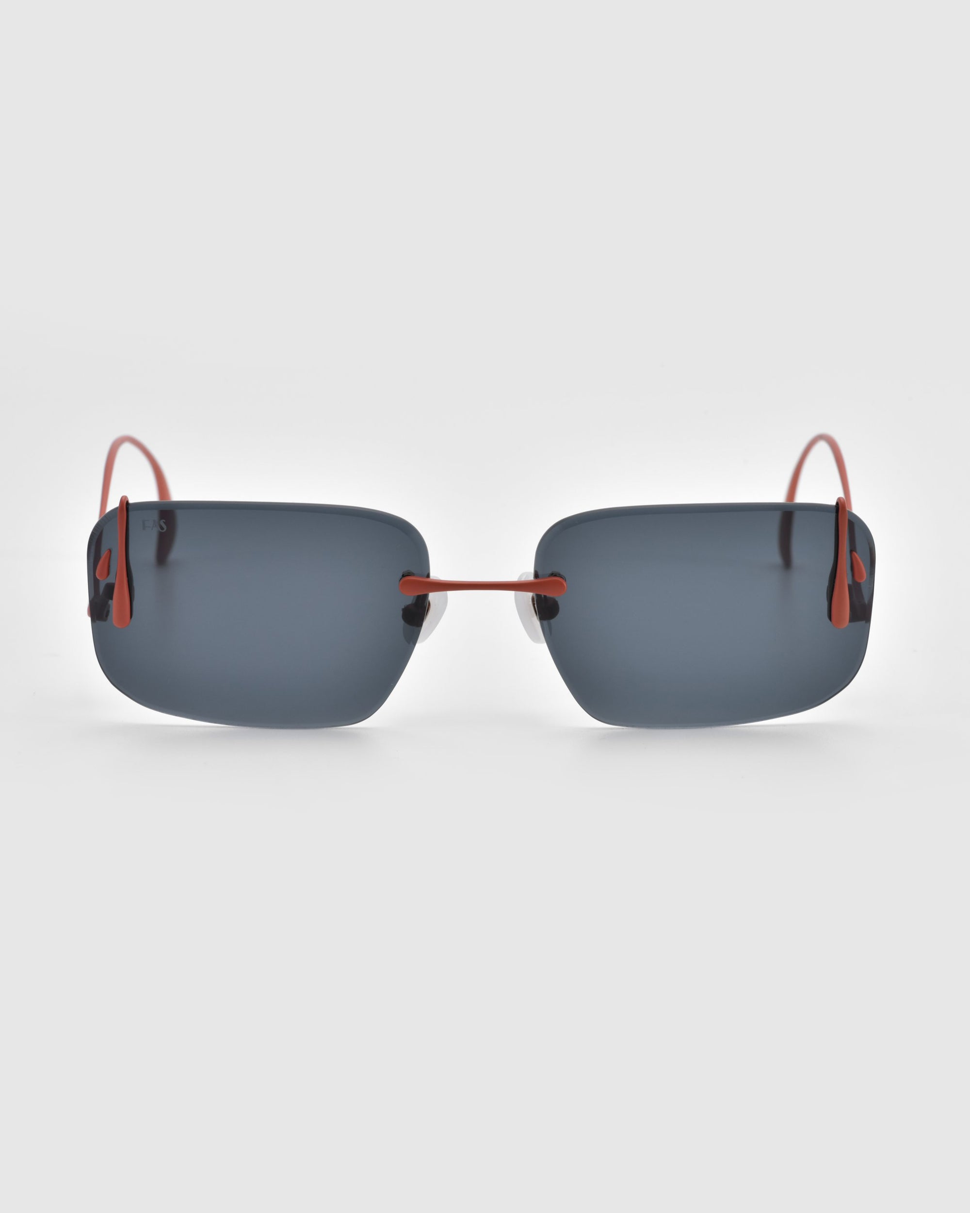 The Vermilion by For Art's Sake® features minimalist rimless sunglasses with rectangular dark-tinted lenses and artistic flair, completed with red wire temples against a plain white background.