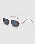 For Art's Sake® presents "Vermilion," sleek rimless sunglasses with rectangular dark lenses and thin red wireframes, combining minimalist appeal with sculptural temples, set against a light gray background.