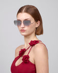 A person with straight, short hair and oversized For Art's Sake® sunglasses with sculptural temples wears the Vermilion red dress featuring floral embellishments on the shoulder straps, posing against a plain backdrop.