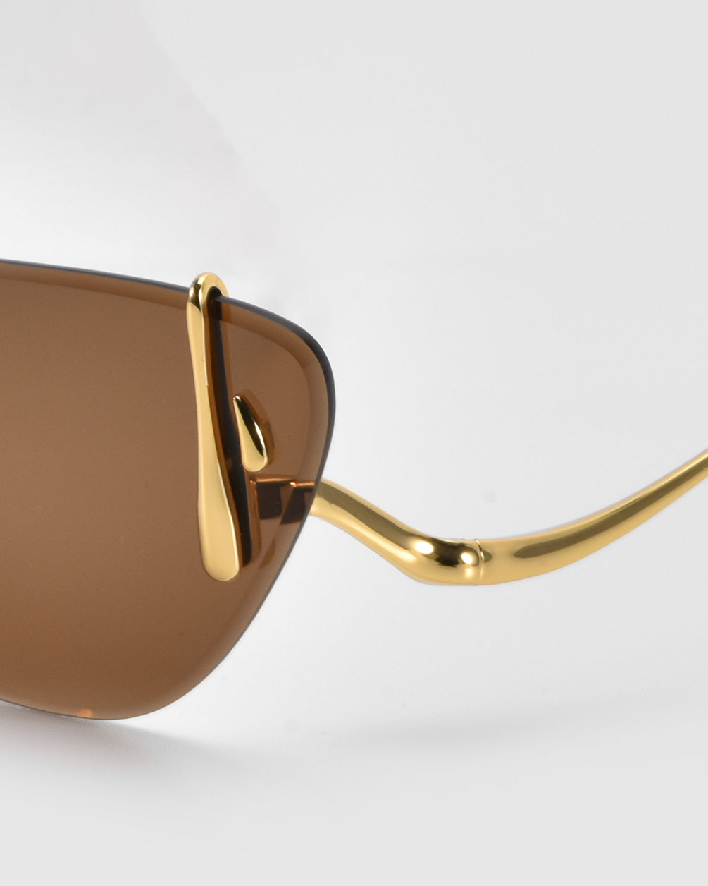 Close-up of Crimson sunglasses by For Art&#39;s Sake® with brown lenses and gold-toned, wavy temples on a white background. Their lightweight design is modern and sleek.