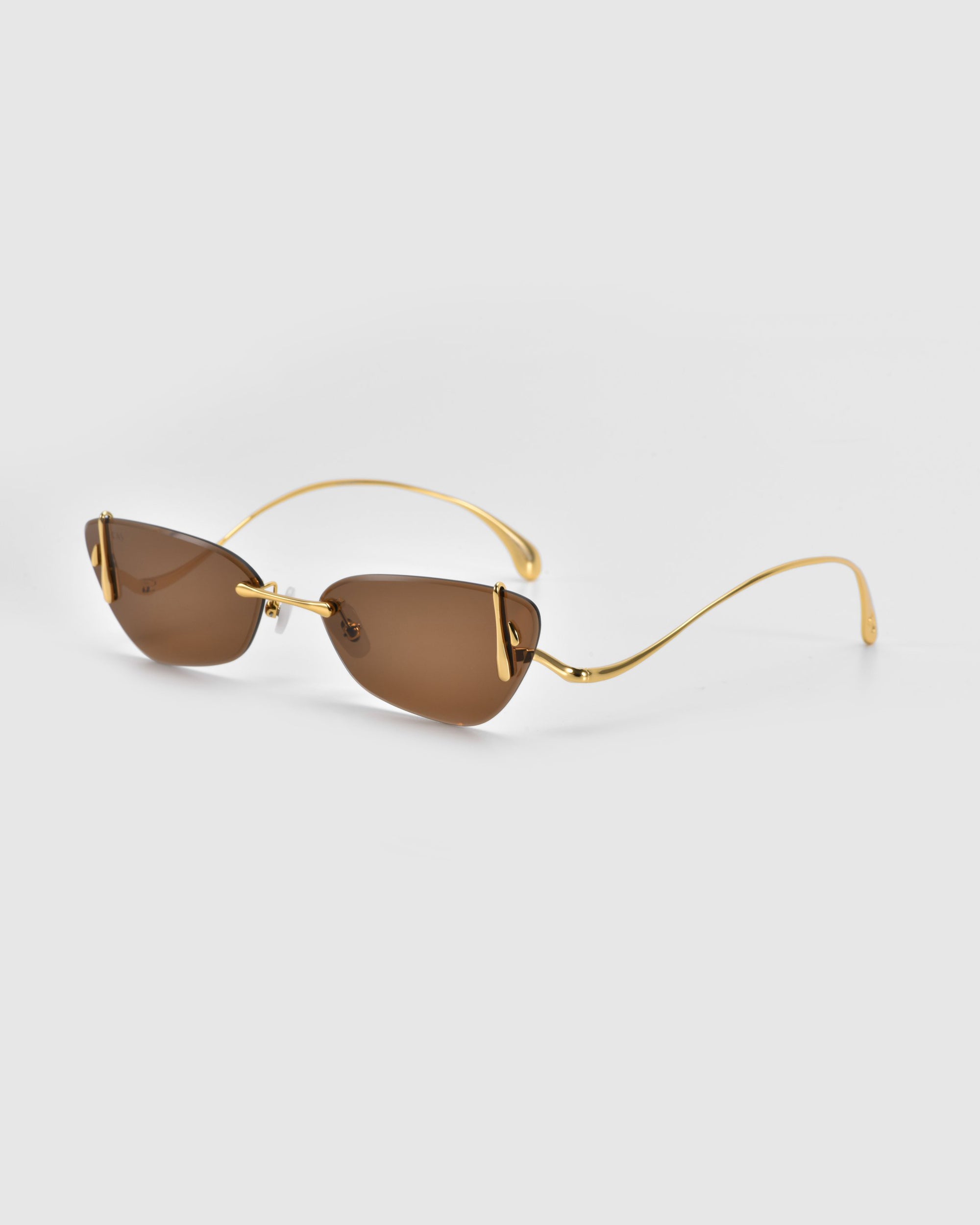 Crimson sunglasses by For Art's Sake® feature a frameless design with gold detail, brown lenses, and sculpted rose ornaments from the Rose Garden Collection. The thin frame adds elegance against a plain white background.