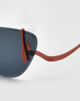 Close-up of For Art's Sake® Crimson sunglasses, showcasing dark blue lenses and orange temples. This lightweight eyewear features a sleek frame with gently curved earpieces against a smooth white background.