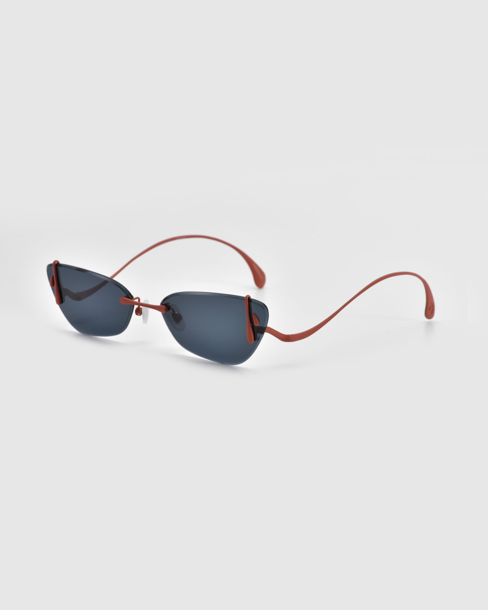 Crimson sunglasses by For Art's Sake® from the Rose Garden Collection boast dark lenses and red frames on a light gray background. This elegant, frameless design features slender red arms enhanced by sculpted rose ornaments for a modern, stylish look.