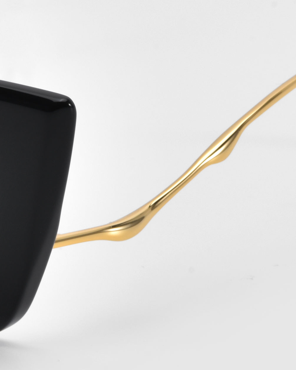 Close-up of For Art's Sake® Dusk glasses with a black acetate frame and sleek gold temple. The unique curve of the temple adds elegance and sophistication, standing out against the white background.