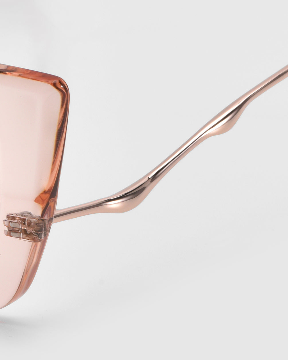 Close-up of For Art's Sake® Dusk eyeglasses featuring pink-tinted lenses and thin rose-gold frames. The sophisticated design showcases a unique waved shape on the temple arm against a plain background.