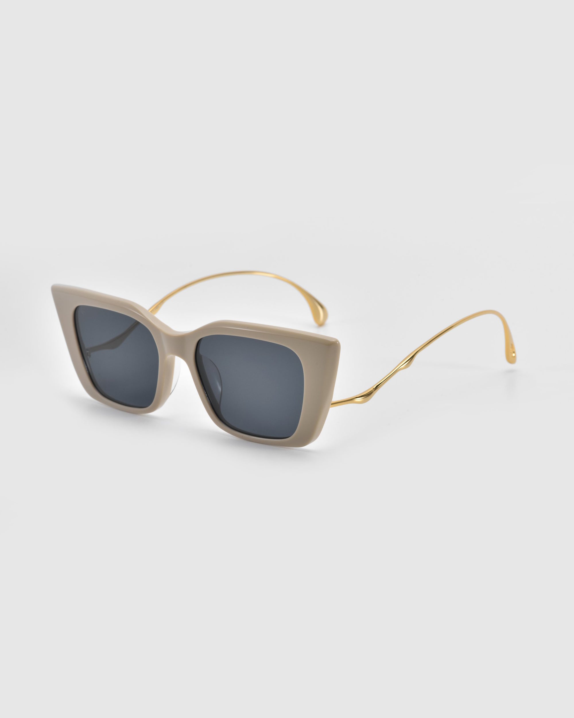 For Art's Sake® Dusk cat-eye sunglasses boast a chic beige silhouette with dark lenses and thin gold arms, set against a light gray background.