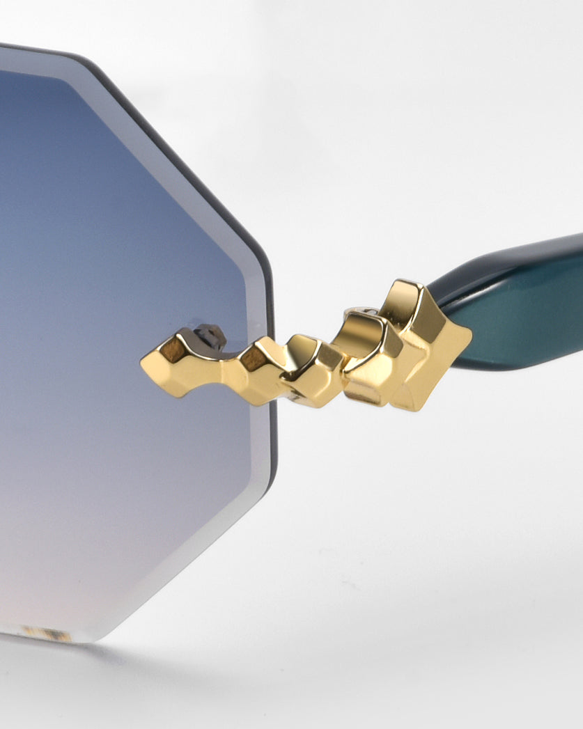 Close-up of For Art's Sake® Haze eyeglass lens with an octagonal shape and silver to blue gradient. It has faceted edging, a decorative gold hinge, and dark green temple arms.