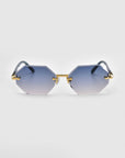 Part of For Art's Sake® Rose Garden collection, the Haze sunglasses feature a hexagonal shape with gradient blue tint, gold-tone hardware, sleek bridge, and subtle temple decorations. Their sophisticated design is showcased by rimless lenses against a plain white background.