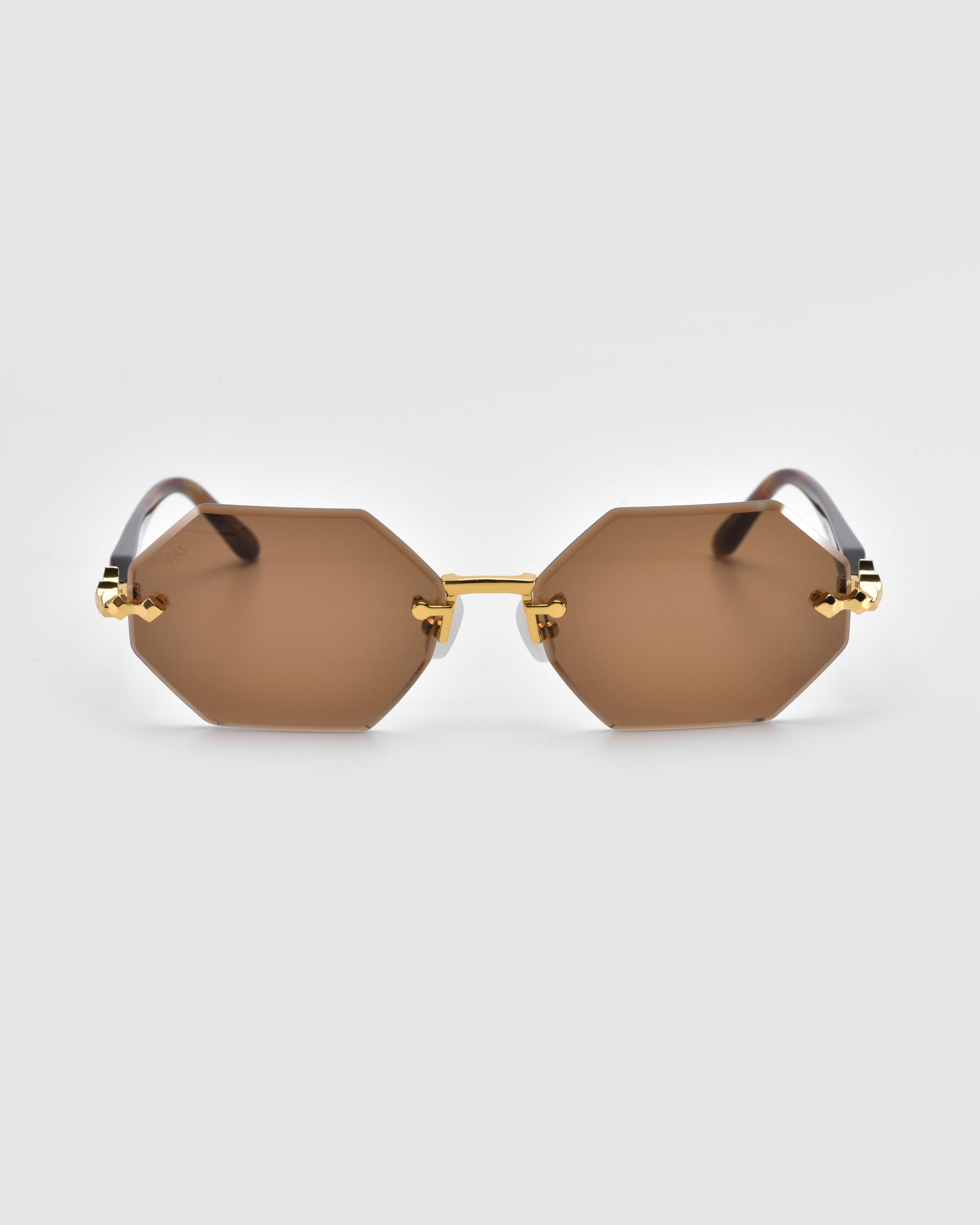 For Art's Sake® presents the 'Haze': hexagonal sunglasses with brown lenses, gold metal frames, and elegant temple decorations, shown from the front against a plain white background.