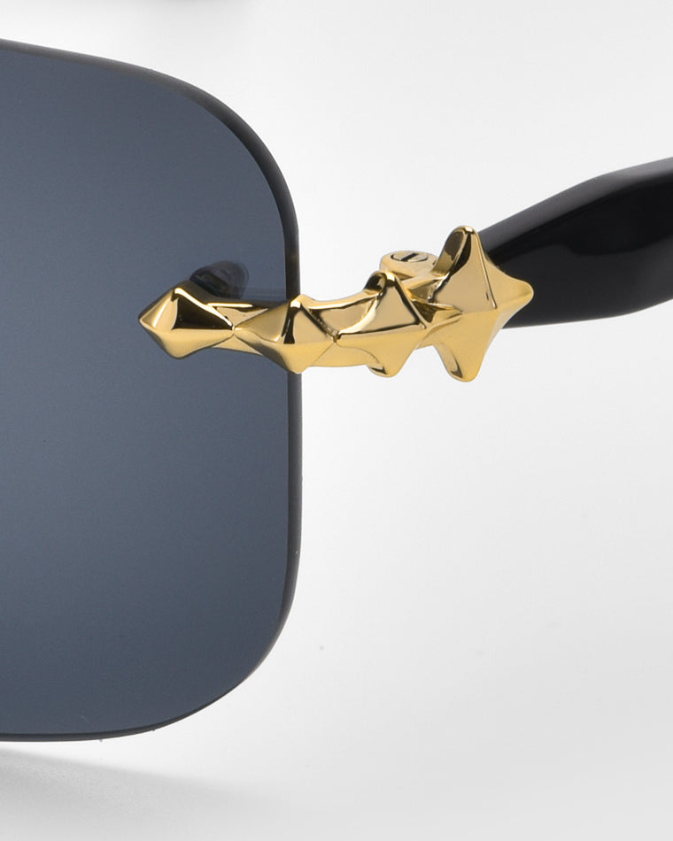 Close-up of the Edith sunglasses by For Art's Sake® showcasing soft rectangular lenses, a black finish, and a unique gold geometric decorative element at the hinge from the Rose Garden collection, adding luxury and modernity to this timeless classic design.