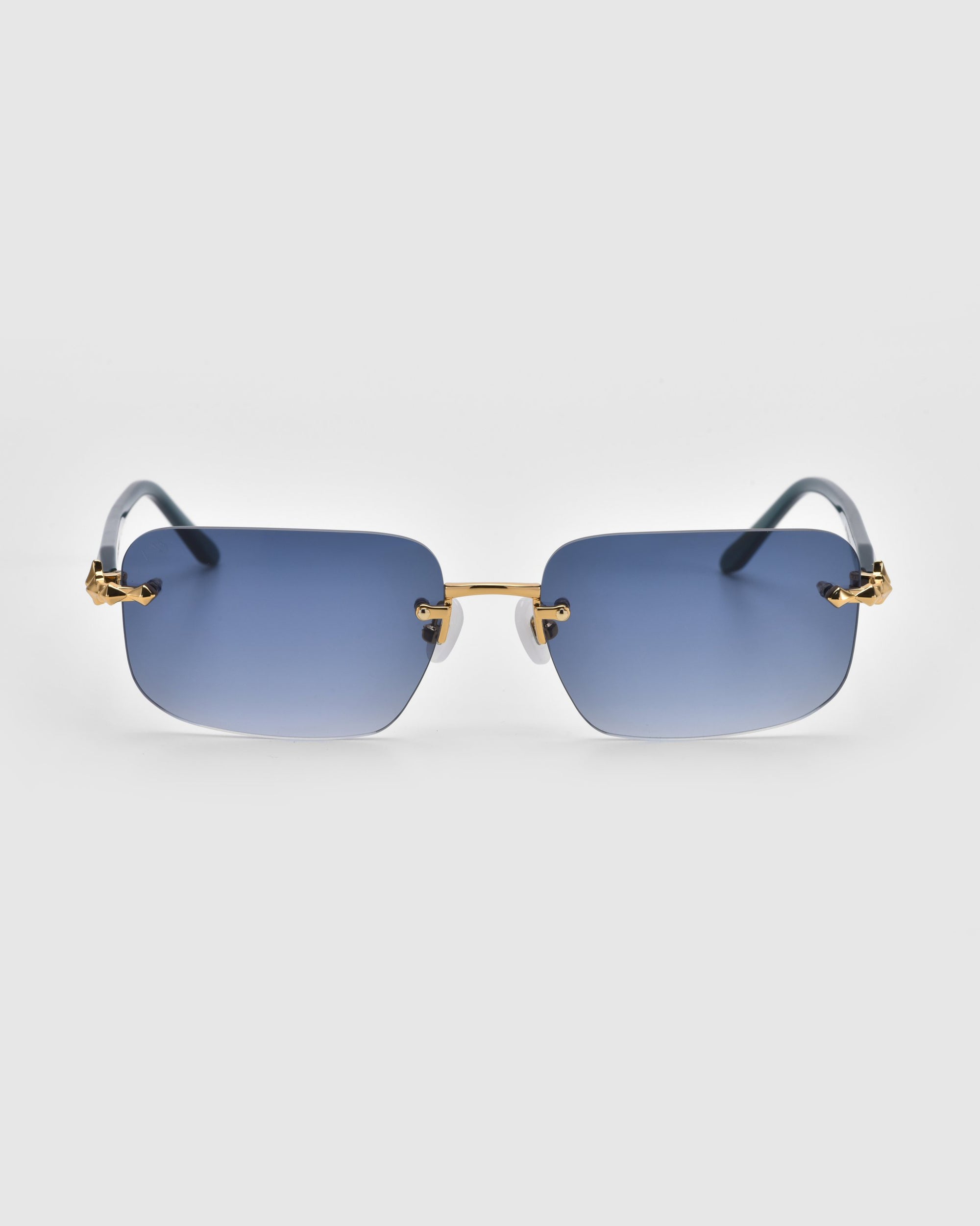 Part of the Rose Garden collection, Edith sunglasses by For Art's Sake® showcase stylish rimless design with blue rectangular lenses and gold accents on the nose bridge and temples, elegantly set against a plain white background.