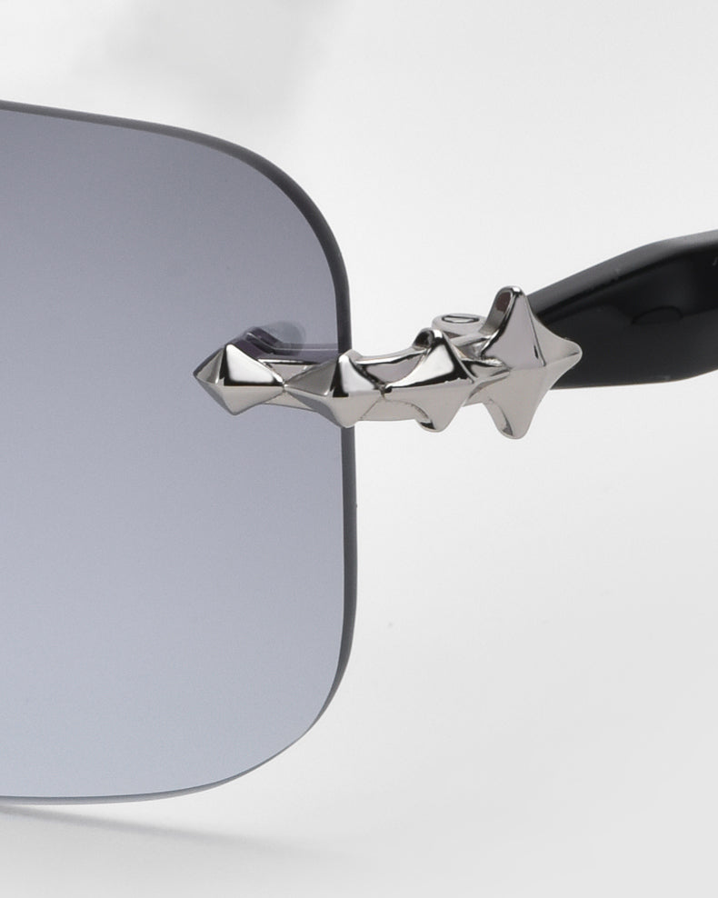 Close-up of For Art's Sake® Edith sunglasses, featuring a black frame and grey rectangular lenses. The arms have a silver star-shaped design near the hinge, part of the Rose Garden collection, emphasizing timeless elegance with unique details.