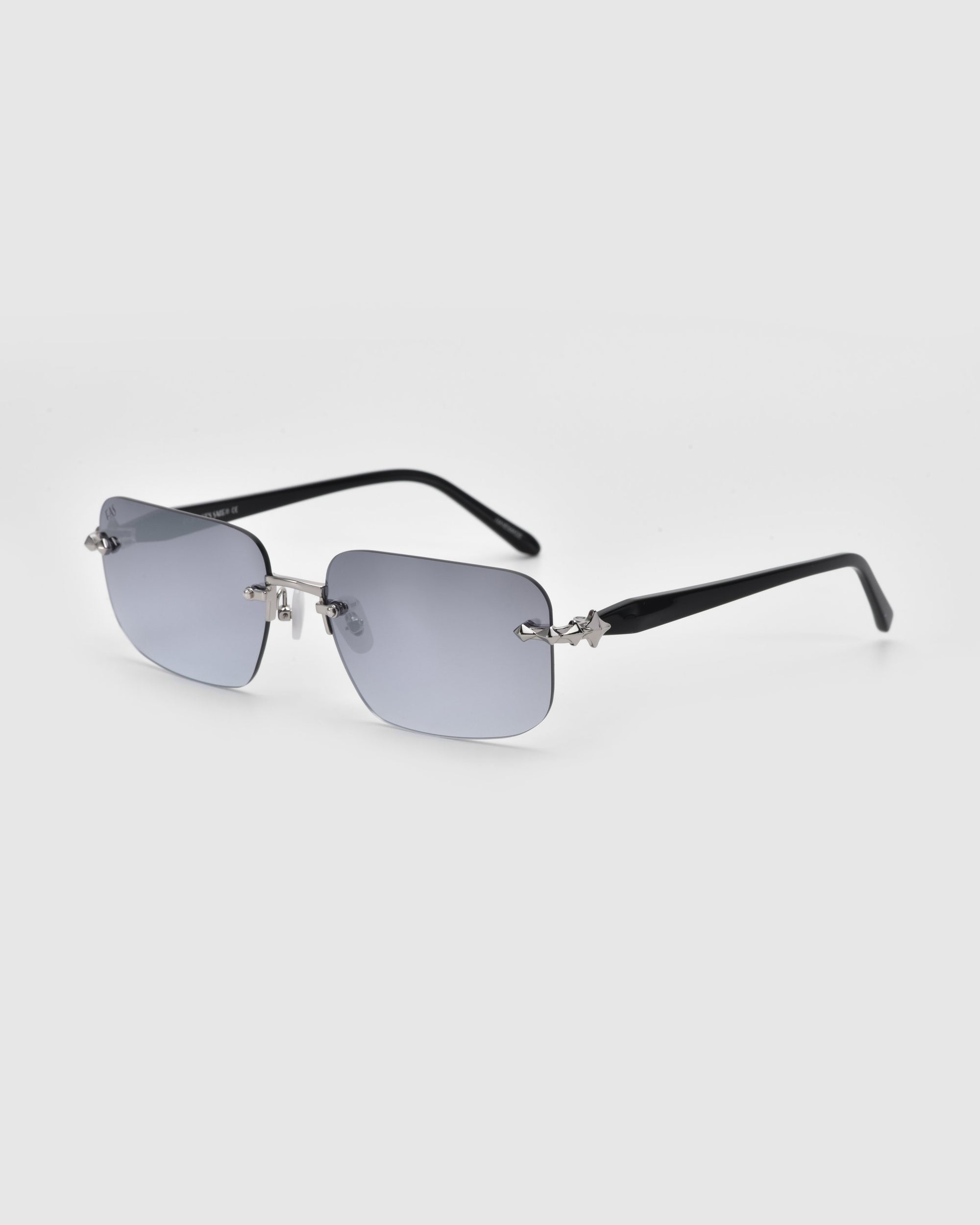 From the For Art's Sake® Rose Garden collection, the Edith rimless rectangular sunglasses boast sleek black temples and grey-tinted lenses against a plain white backdrop.