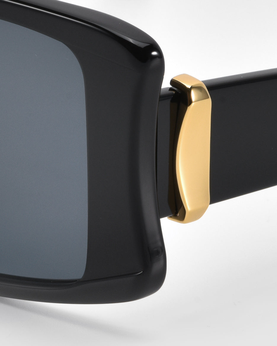 The Bloom sunglasses by For Art's Sake® feature an oversized black acetate frame with a glossy finish and bold gold-tone accents on the temple. The dark lenses contrast elegantly with the sleek design, showcasing premium craftsmanship and modern style.