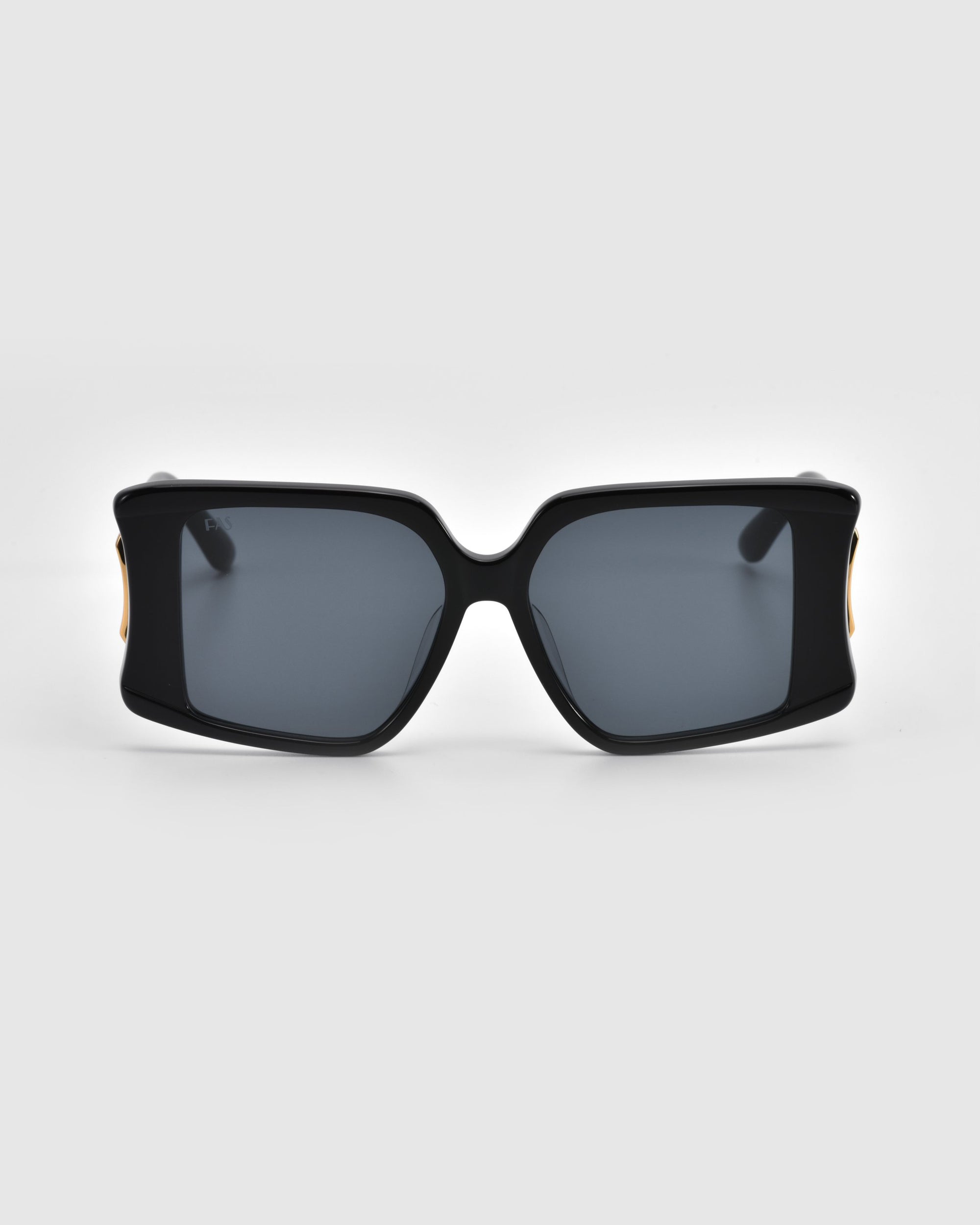 The Bloom sunglasses by For Art's Sake® feature bold rectangular black frames with dark lenses and jewelry-like gold accents on the sides, enhancing their glossy design against a soft gray background.