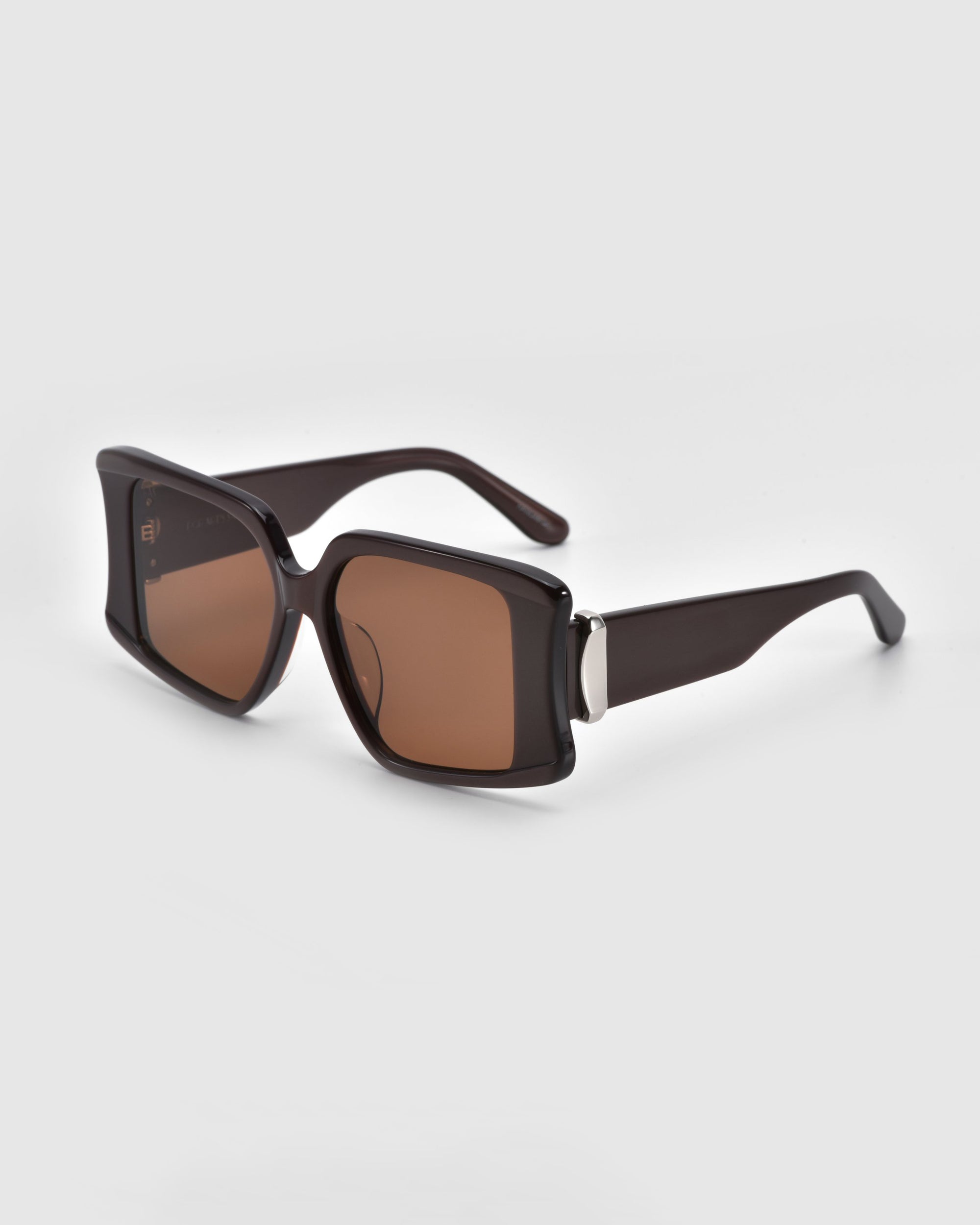 The Bloom sunglasses by For Art's Sake® feature sleek brown tones with square lenses and oversized acetate frames, boldly set against a light gray background.