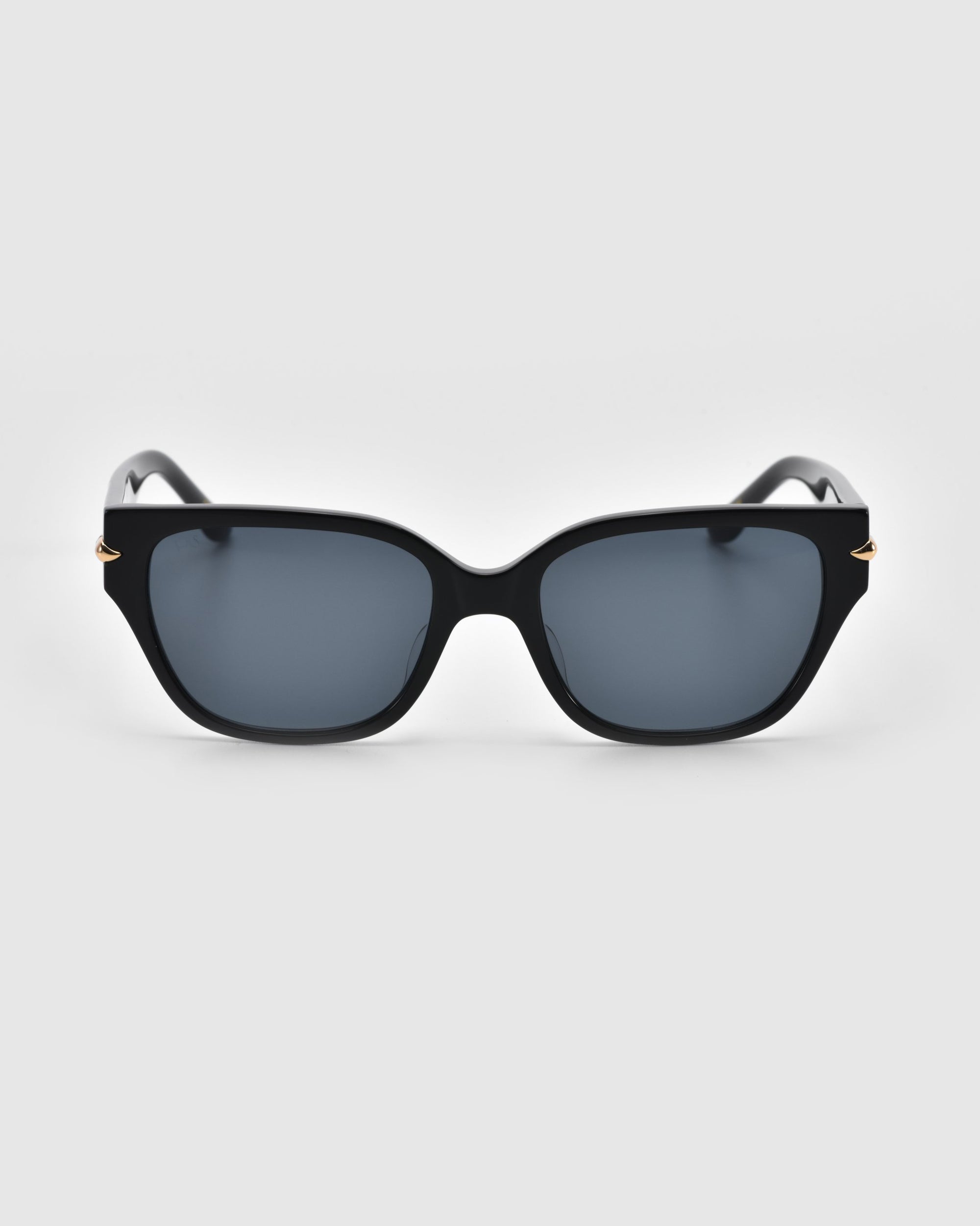 A pair of For Art's Sake® Rosie sunglasses, featuring a black rectangular design with dark lenses and small gold accents on the sides, viewed from the front against a plain white background.