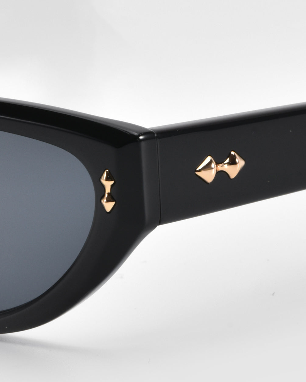 Close-up of Lush cat-eye sunglasses by For Art's Sake®, showcasing gold arrow details on the black frame. The dark-tinted lenses emphasize the stylish design against a neutral background.