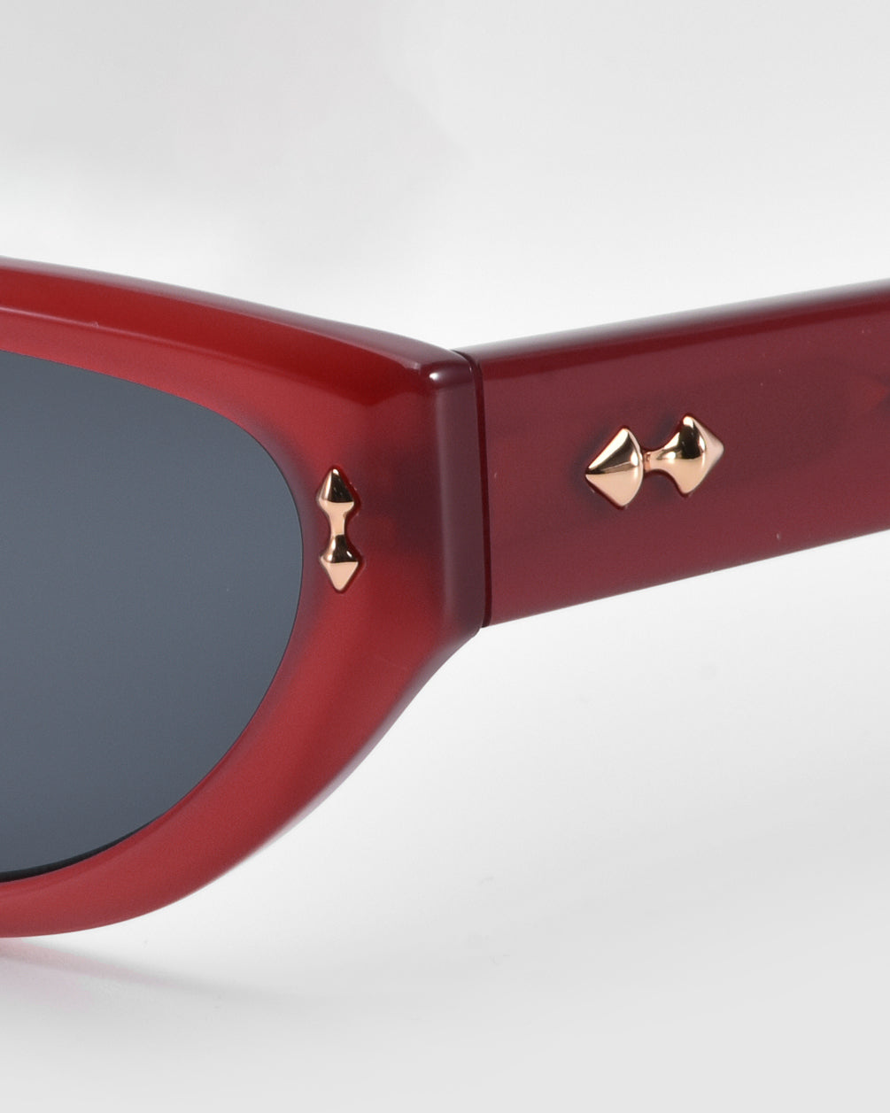 Close-up of For Art's Sake® Lush sunglasses featuring a glossy red frame with geometric facets. The temple arm has two gold pyramid studs near the hinge, and the dark lenses contrast beautifully with the vibrant red, highlighting the premium materials used in their design.