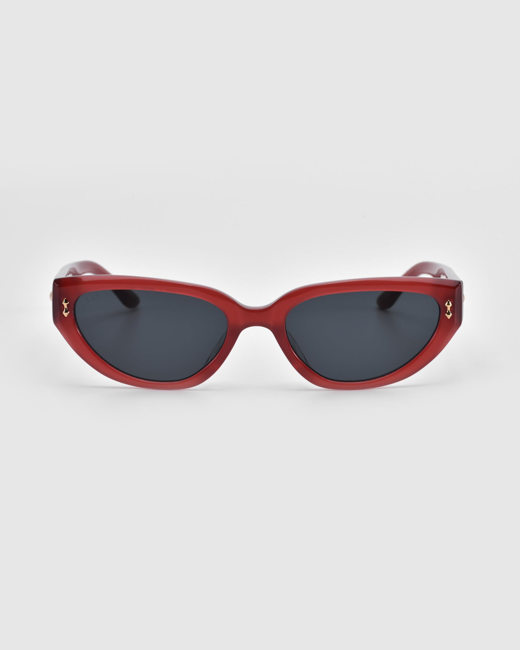 The Lush cat-eye sunglasses by For Art's Sake® feature red frames with dark lenses, crafted from premium materials, and are showcased against a plain white background.