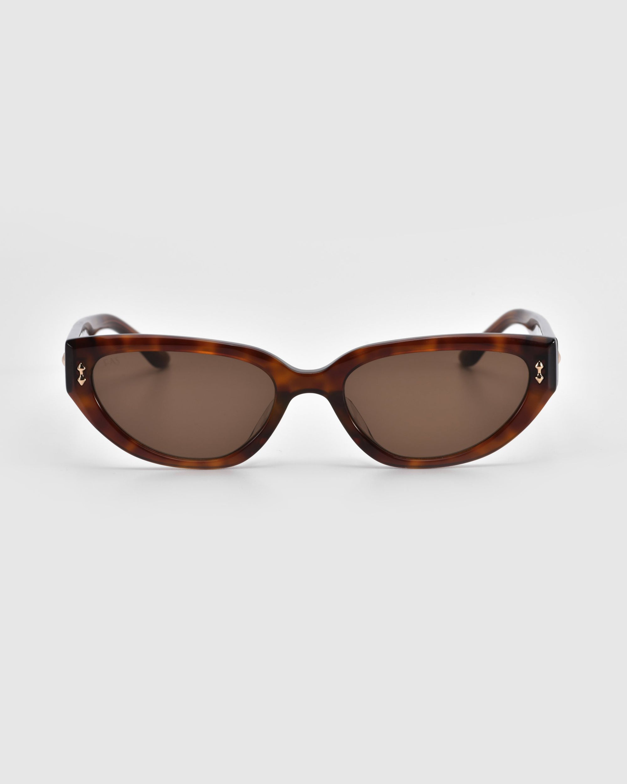 The Lush sunglasses by For Art's Sake® feature tortoiseshell curved rectangular frames and brown lenses, crafted from premium materials. Displayed on a white background, each temple is accented with a small metallic decoration.