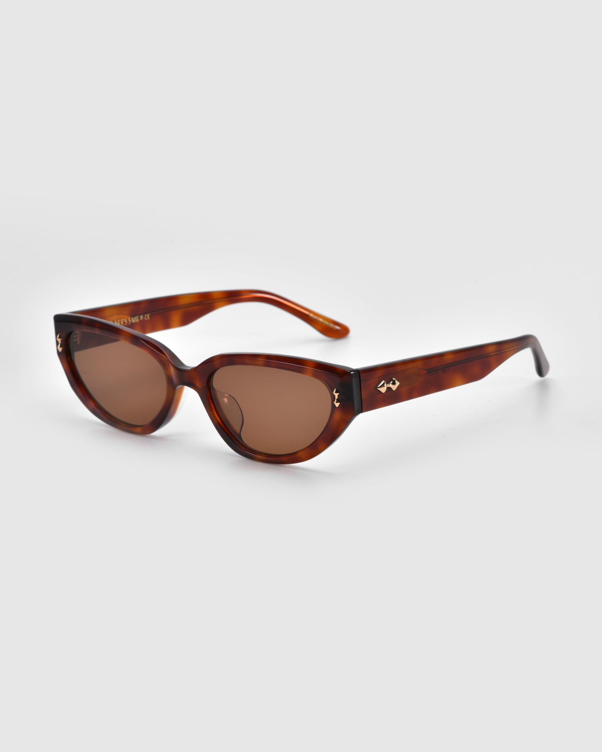 The Lush sunglasses by For Art's Sake® feature a cat-eye style with tortoiseshell frames, brown tinted lenses, and a stylized logo on the temples. Crafted from premium full acetate, they stand out against the light gray background.