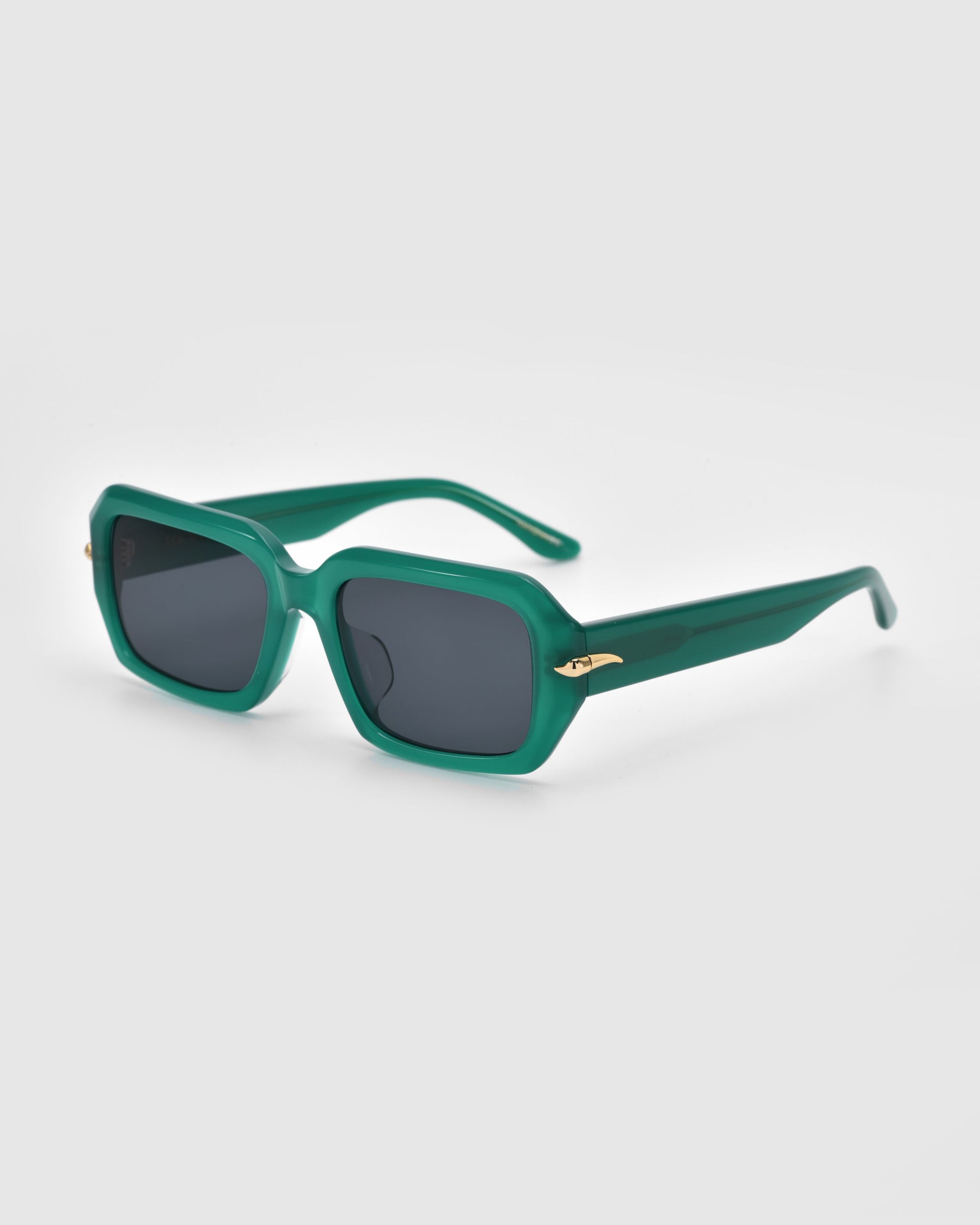 Fleur sunglasses by For Art's Sake® feature a sleek green acetate frame, dark lenses, and gold-accented temples against a plain light gray background.