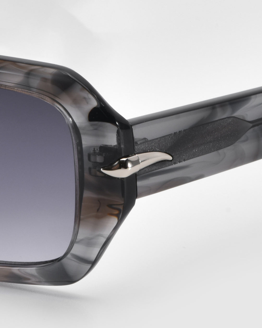 Close-up of the Fleur sunglasses by For Art's Sake® featuring a marbled gray frame and gradient dark lenses. The minimalist design includes a small metallic arrow on the temple, adding a distinctive touch.