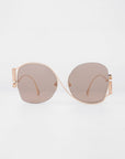 A pair of For Art's Sake® Sapphire sunglasses with large, light brown lenses and thin, gold-colored frames. The Sapphire sunglasses, offering UV protection, are positioned symmetrically against a plain white background.