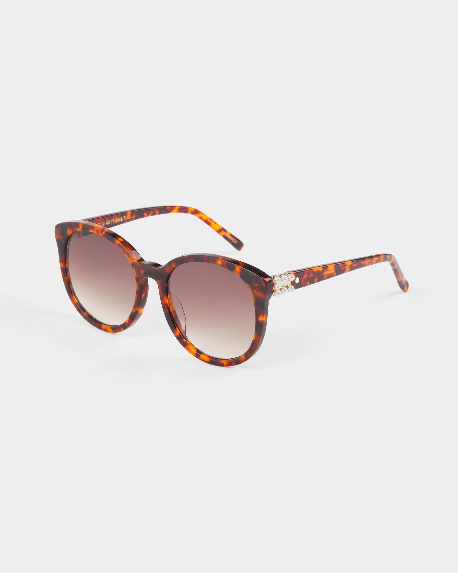 A pair of For Art&#39;s Sake® Scarlett tortoiseshell sunglasses with round, shatter-resistant nylon lenses that offer UVA &amp; UVB protection. The temples of the sunglasses feature decorative gold accents, and the frames have an elegant brown and amber mottled pattern, set against a plain white background.