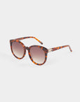 A pair of For Art's Sake® Scarlett tortoiseshell sunglasses with round, shatter-resistant nylon lenses that offer UVA & UVB protection. The temples of the sunglasses feature decorative gold accents, and the frames have an elegant brown and amber mottled pattern, set against a plain white background.
