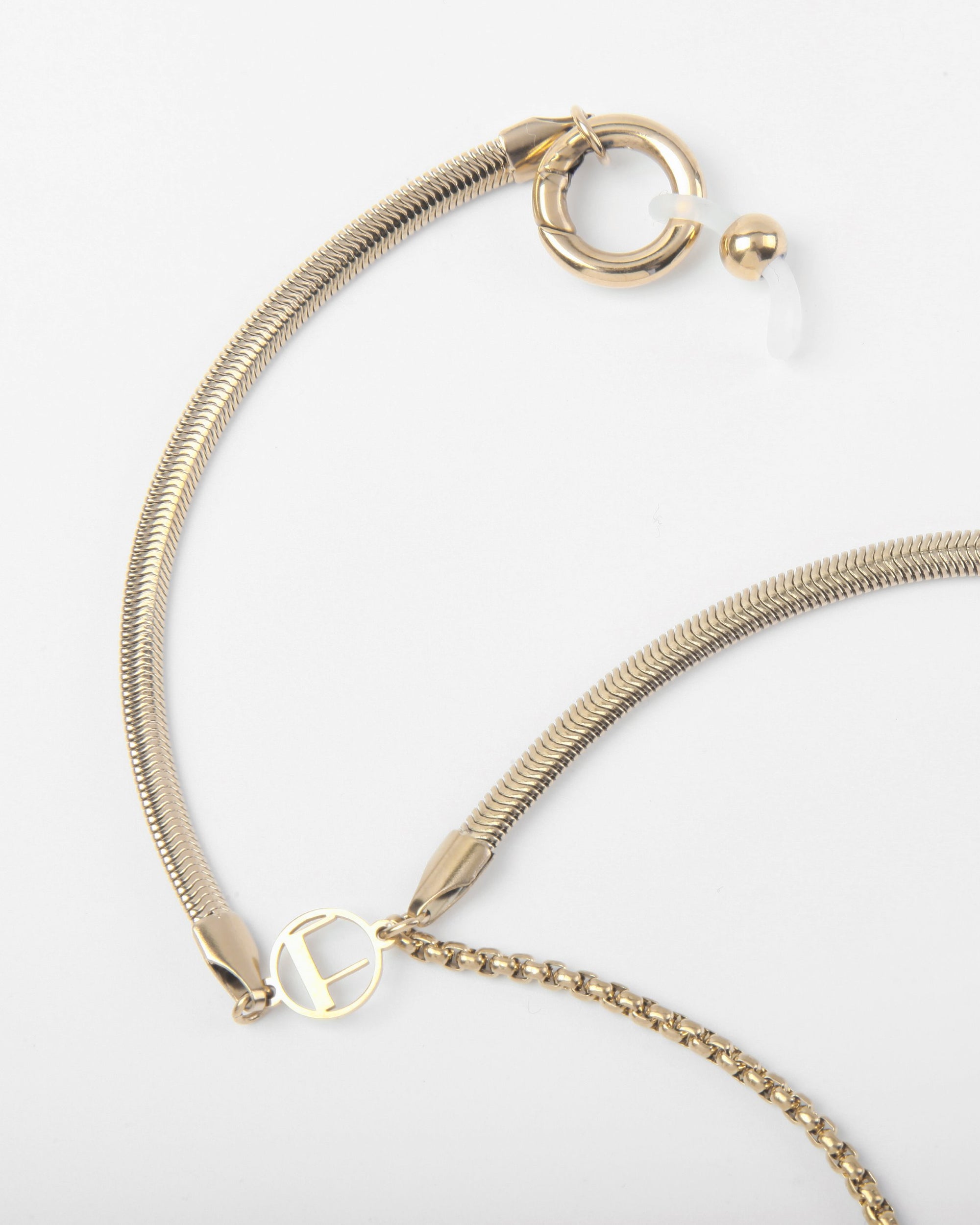 A Snake Glasses Chain with a flexible, textured band and decorative elements, including a round charm with a cutout design, small loop, and larger circular clasp with a bead end. The Snake Glasses Chain lies against a plain white background, reminiscent of the intricate craftsmanship seen in For Art's Sake® necklaces.