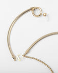 A Snake Glasses Chain with a flexible, textured band and decorative elements, including a round charm with a cutout design, small loop, and larger circular clasp with a bead end. The Snake Glasses Chain lies against a plain white background, reminiscent of the intricate craftsmanship seen in For Art's Sake® necklaces.