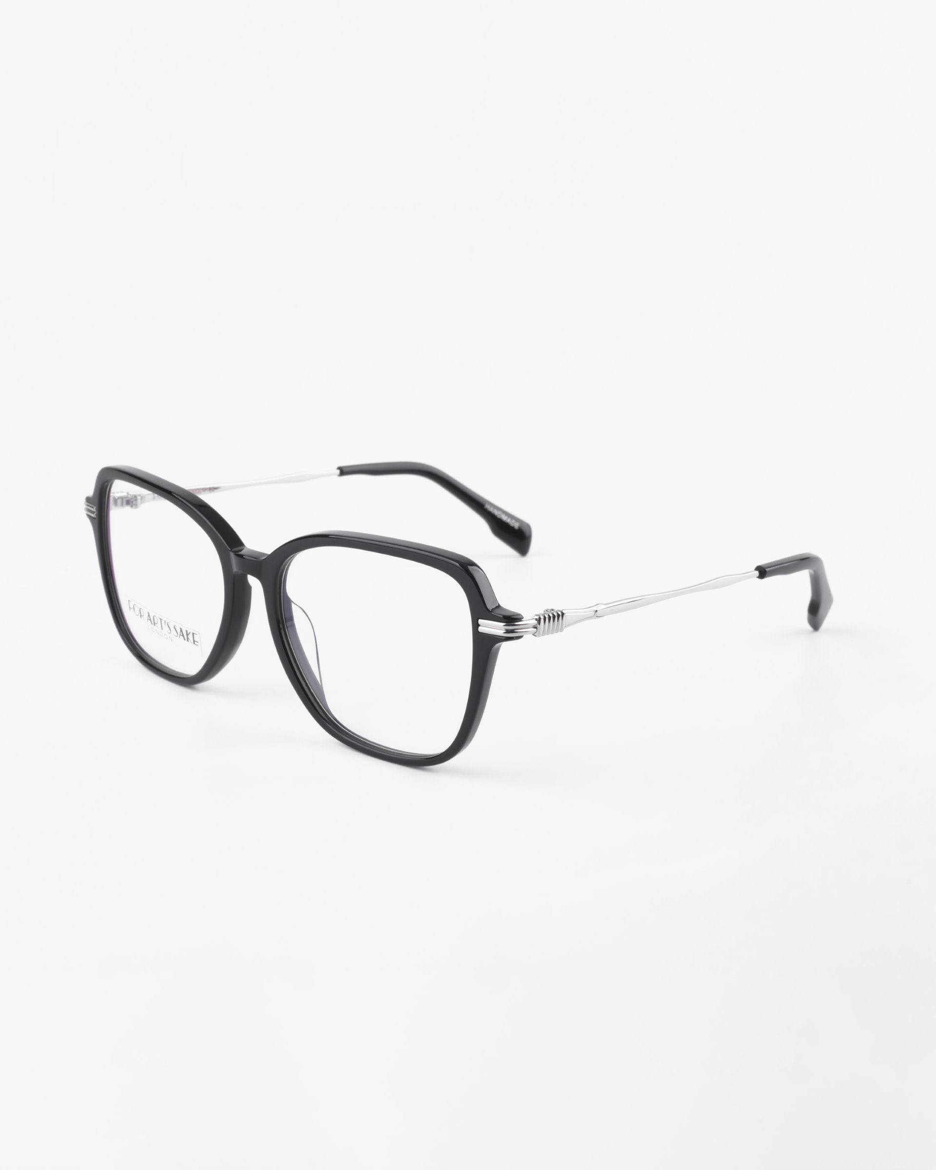A pair of black, rectangular Sonnet eyeglasses from For Art&#39;s Sake® with a thin silver frame around the lenses. The arms are black at the tips with a spring hinge detail near the frame. Featuring blue light filter for added eye protection, the glasses are positioned on a white surface.