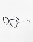 A pair of black, rectangular Sonnet eyeglasses from For Art's Sake® with a thin silver frame around the lenses. The arms are black at the tips with a spring hinge detail near the frame. Featuring blue light filter for added eye protection, the glasses are positioned on a white surface.