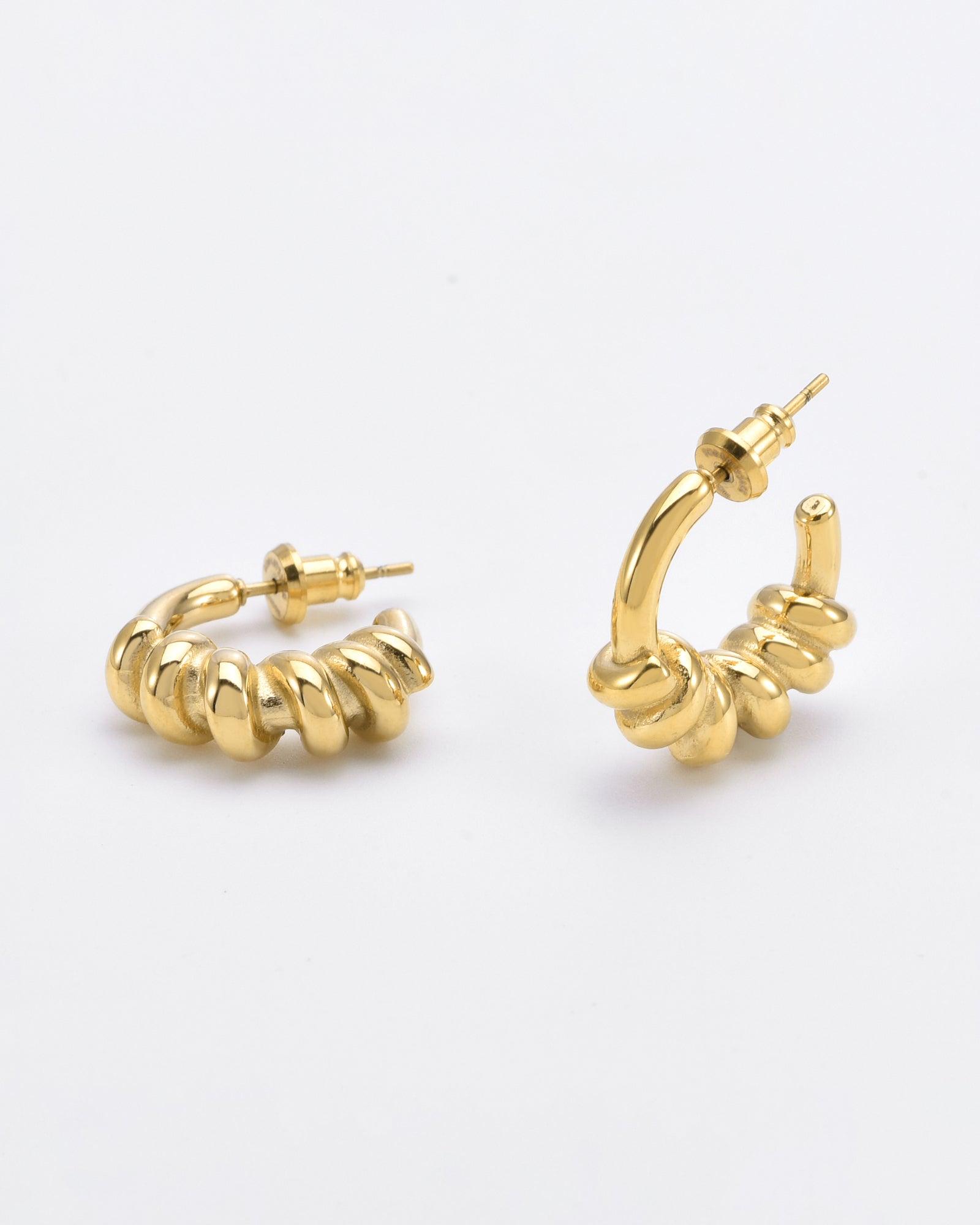 A pair of Swirl Earrings Gold by For Art's Sake® with a unique spiral design. These hypoallergenic earrings have a glossy finish and are displayed on a plain white background. One earring is resting on its side, while the other stands upright, showing the stud and back closure.