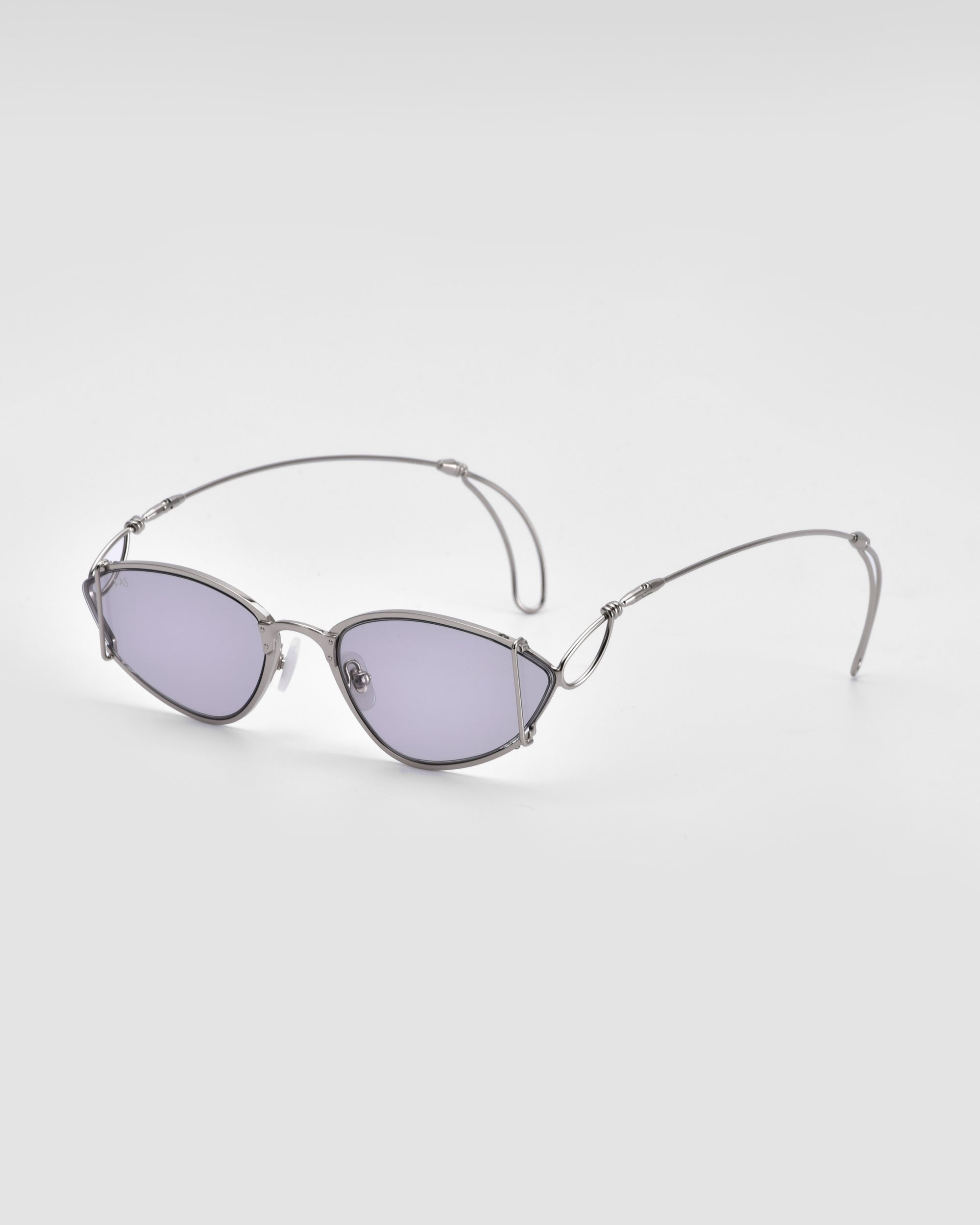 The Ornate sunglasses from For Art&#39;s Sake® feature thin, silver metallic frames and oval-shaped, lightly tinted lenses that offer 100% UVA &amp; UVB protection. The arms are curved at the ends and showcase intricate metal detailing near the hinges, set against a plain white background.