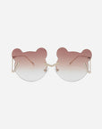 A pair of For Art's Sake® Teddy sunglasses with unique, bear-ear-shaped frames. The gradient lenses transition from a dark rose color at the top to clear at the bottom. The minimal stainless steel frames feature gold-toned temples and adjustable nosepads for added comfort and UV protection.