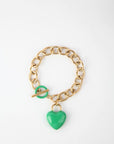 A pendant bracelet with large, interconnected 18k gold links is shown on a white background. It features a toggle clasp and an enamel-covered green heart-shaped charm. This is "The Kiss Bracelet" by For Art's Sake®.