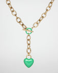 A gold necklace with a clasp and a green enamel-coated heart-shaped pendant. The Kiss Necklace Pink by For Art's Sake® features large interlocking links and a toggle closure, with the vibrant heart hanging at the center of the chain on a short length of additional links.