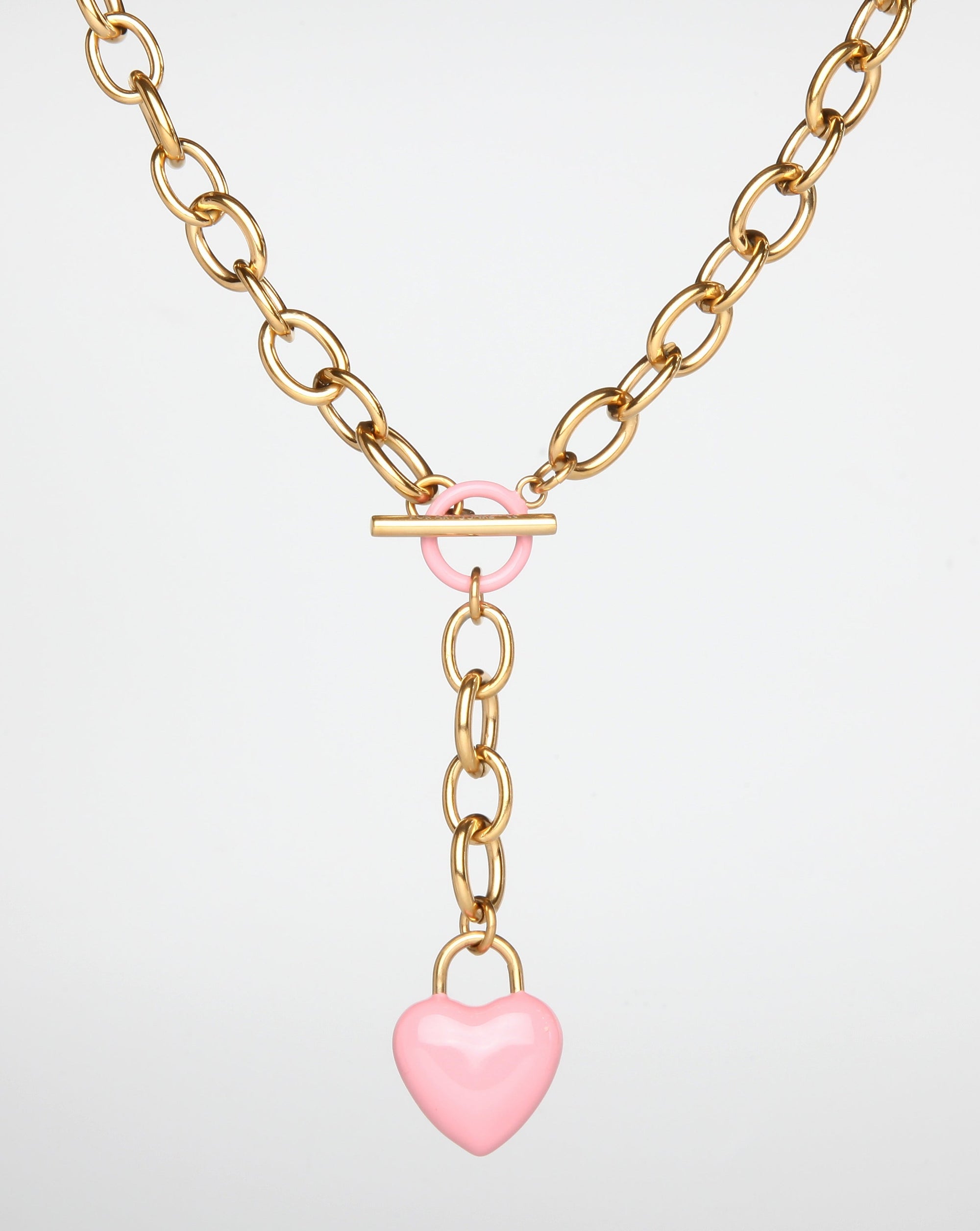 The Kiss Necklace Pink by For Art's Sake® features a pink, enamel-coated heart-shaped pendant hanging from a central T-bar clasp, which is also adorned with a pink ring.