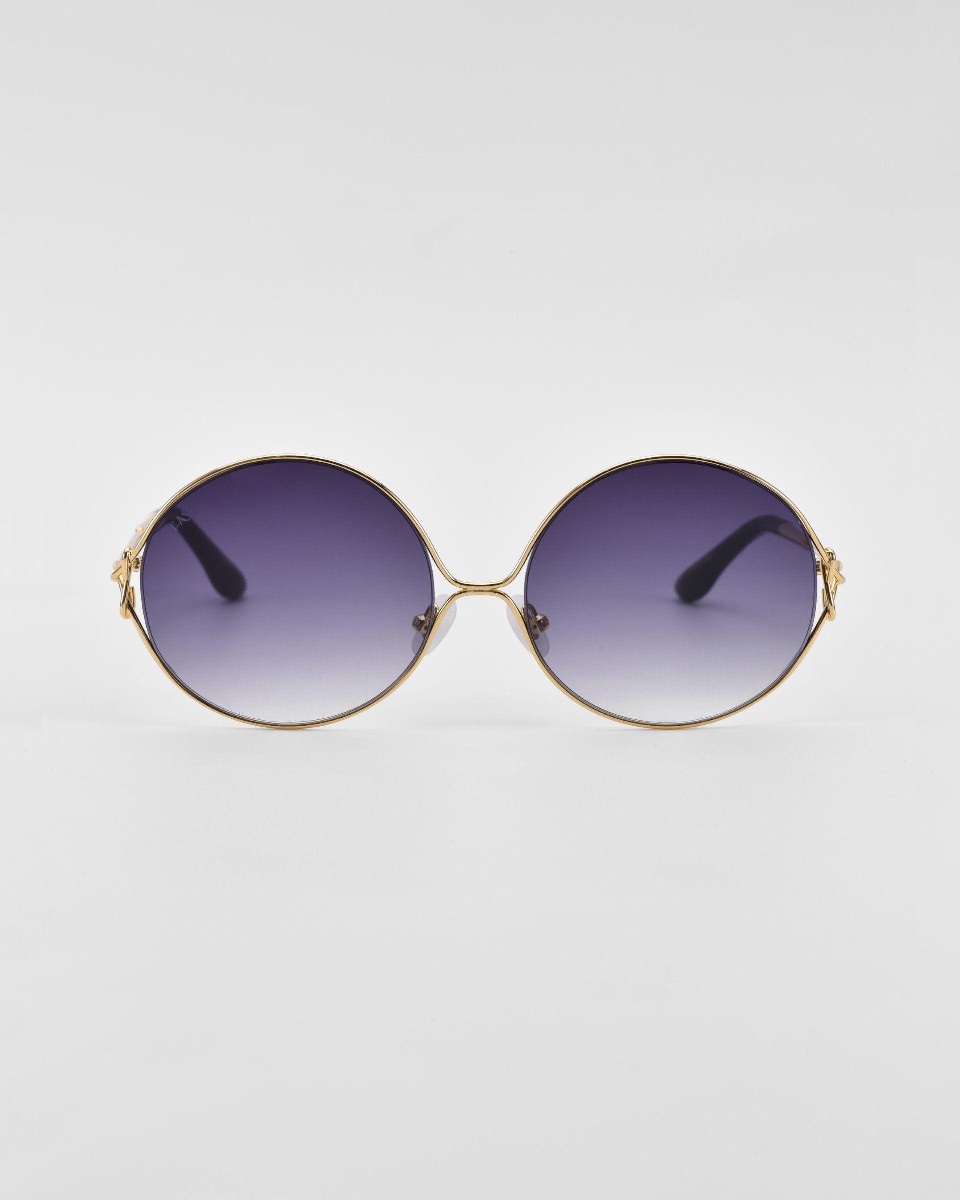 A pair of retro-inspired Aura sunglasses by For Art&#39;s Sake® with oversized round gold frames and purple gradient lenses. The temples are adorned with small decorative elements near the hinges, set against a plain white background.