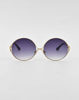 A pair of retro-inspired Aura sunglasses by For Art's Sake® with oversized round gold frames and purple gradient lenses. The temples are adorned with small decorative elements near the hinges, set against a plain white background.