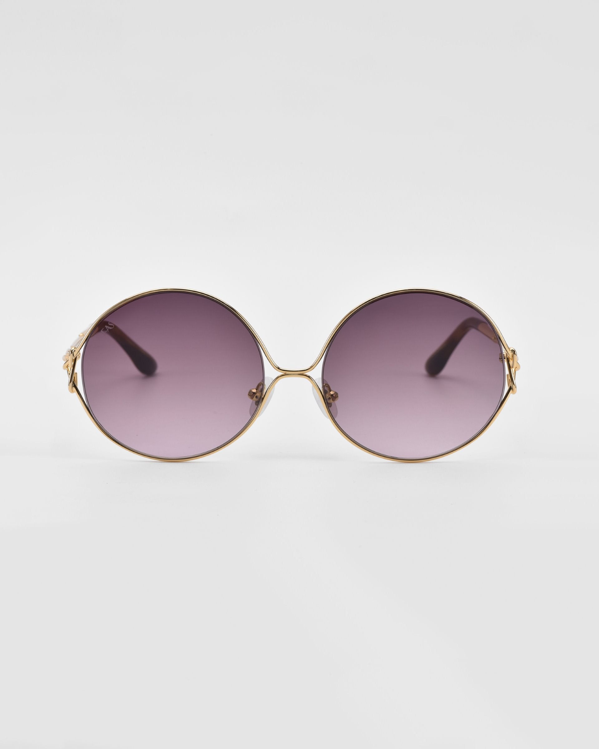 A pair of stylish, retro-inspired For Art's Sake® Aura sunglasses with oversized round gold frames and dark, gradient purple lenses. The edges of the frames feature decorative gold accents. The background is plain white.