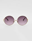 A pair of stylish, retro-inspired For Art's Sake® Aura sunglasses with oversized round gold frames and dark, gradient purple lenses. The edges of the frames feature decorative gold accents. The background is plain white.