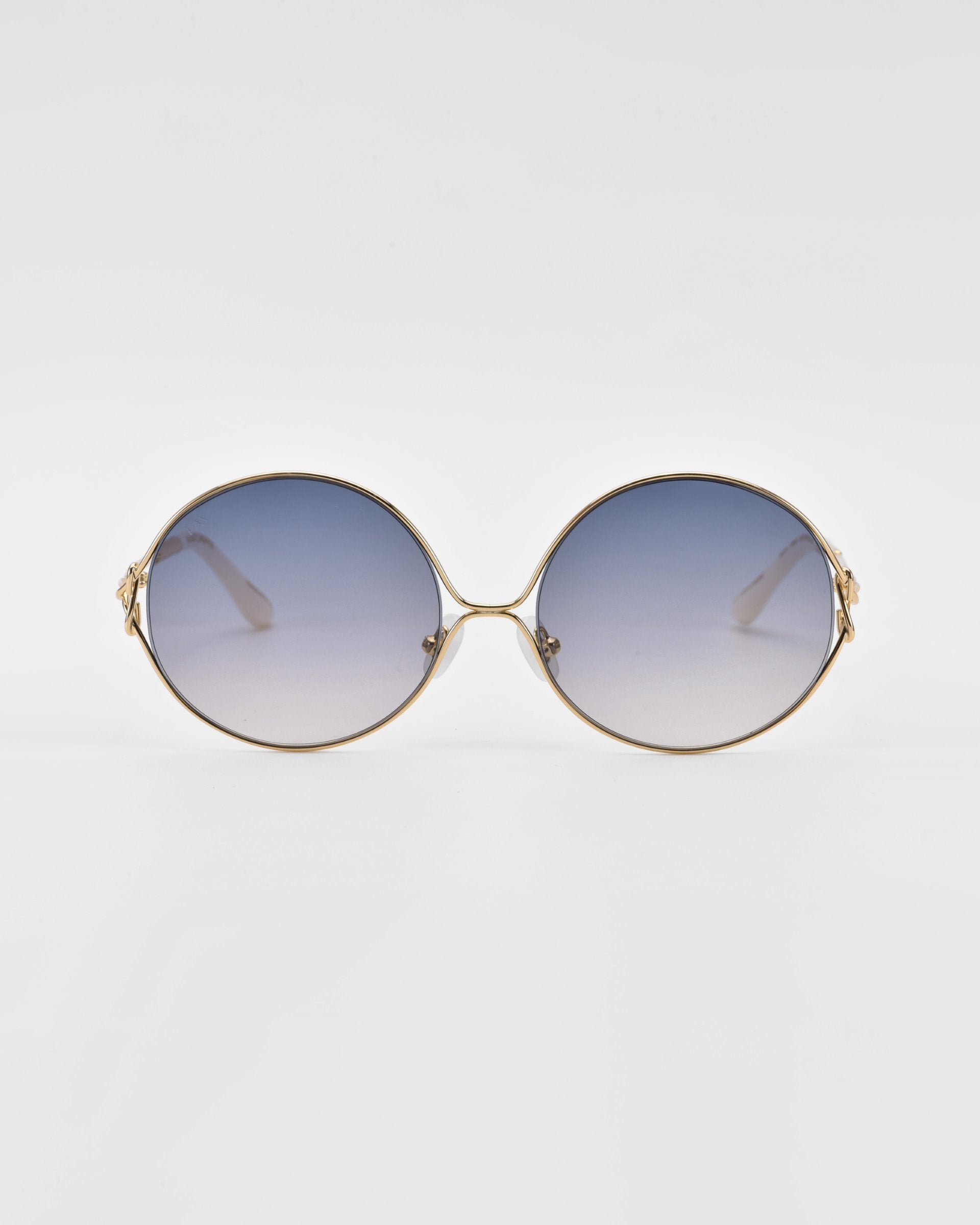 A pair of stylish retro-inspired sunglasses featuring oversized round frames and gradient tinted lenses. The lenses transition from dark blue at the top to a lighter shade towards the bottom. The backdrop is minimal and white. The product name is Aura and it is by For Art&#39;s Sake®.